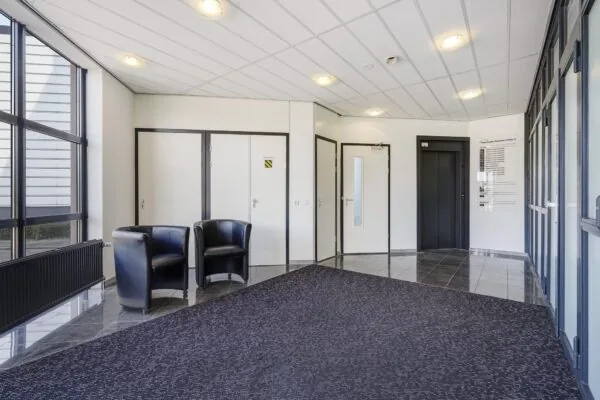 Moderne ontvangsthal van een kantoorpand aan de Laan van 's-Gravenmade met zwarte stoelen, lift en binnendeuren.